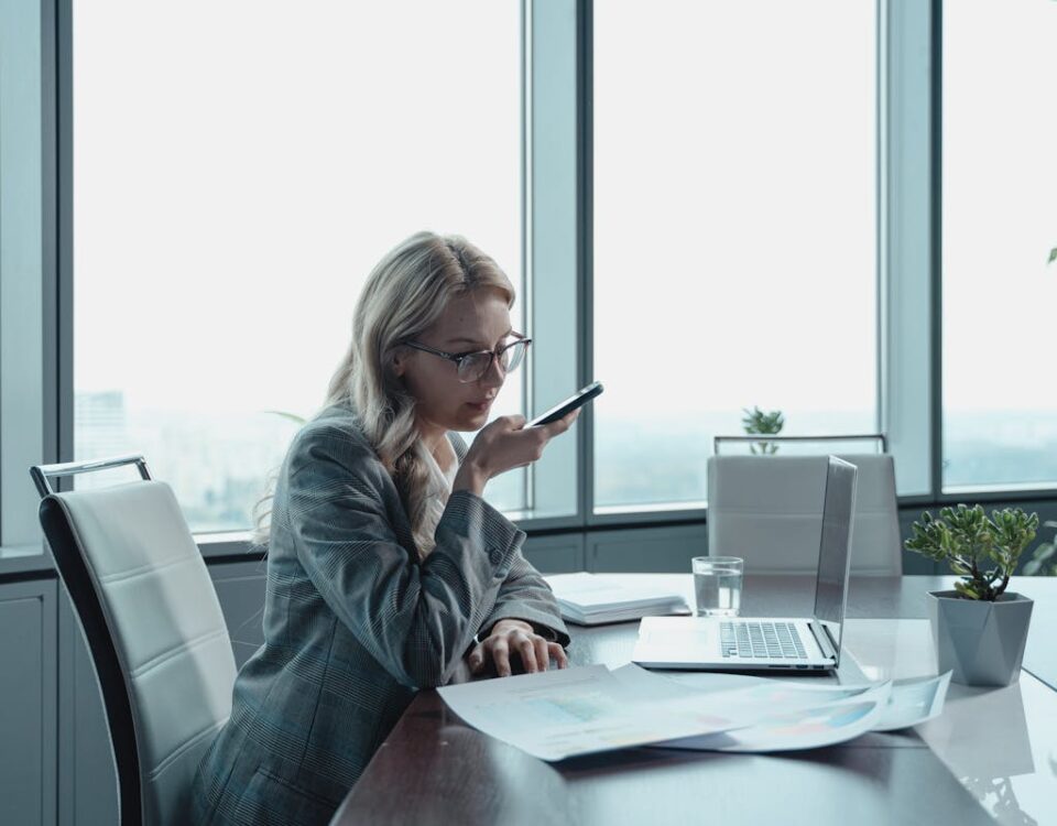 Gestão de estoque que melhora o e-commerce Businesswoman using phone in modern office with laptop and documents.