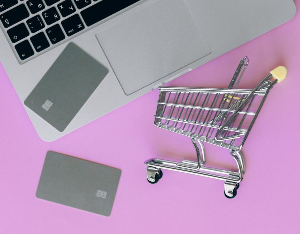 Como evitar problemas nas compras online de produtos caros A minimalist flat lay of a credit card, laptop, and miniature shopping cart.