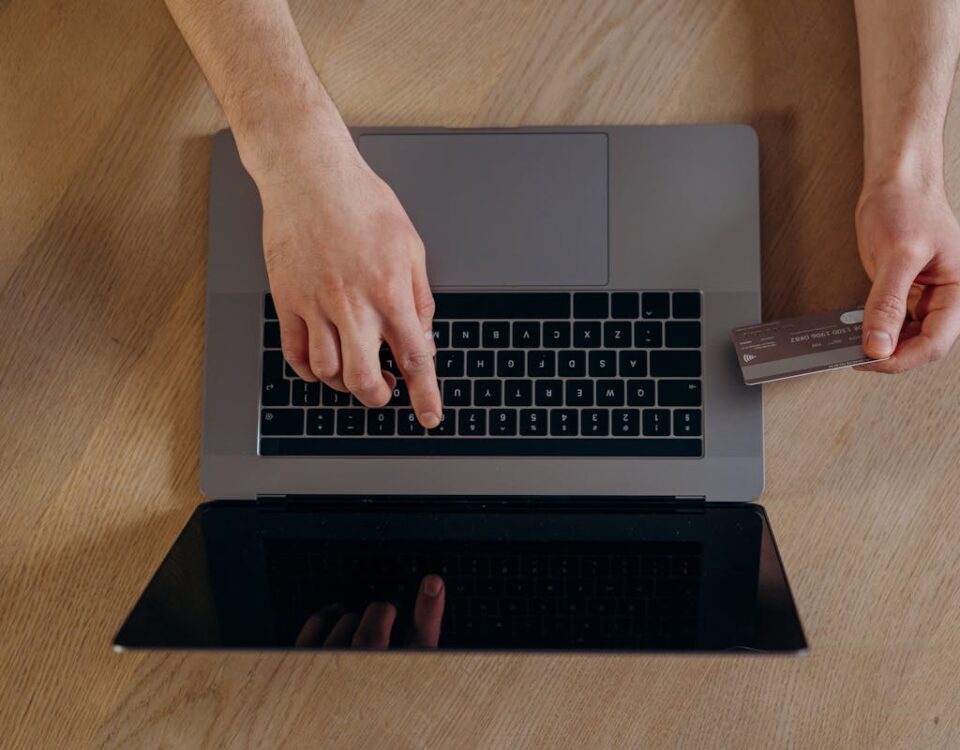 Como escolher meios de pagamento no e-commerce Top view of hands using a credit card and laptop for online transactions on a wooden surface.