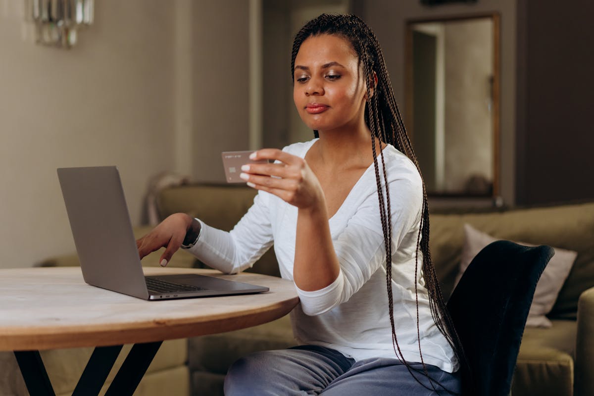 A woman sits indoors shopping online with her laptop and credit card, showcasing modern technology and convenience.