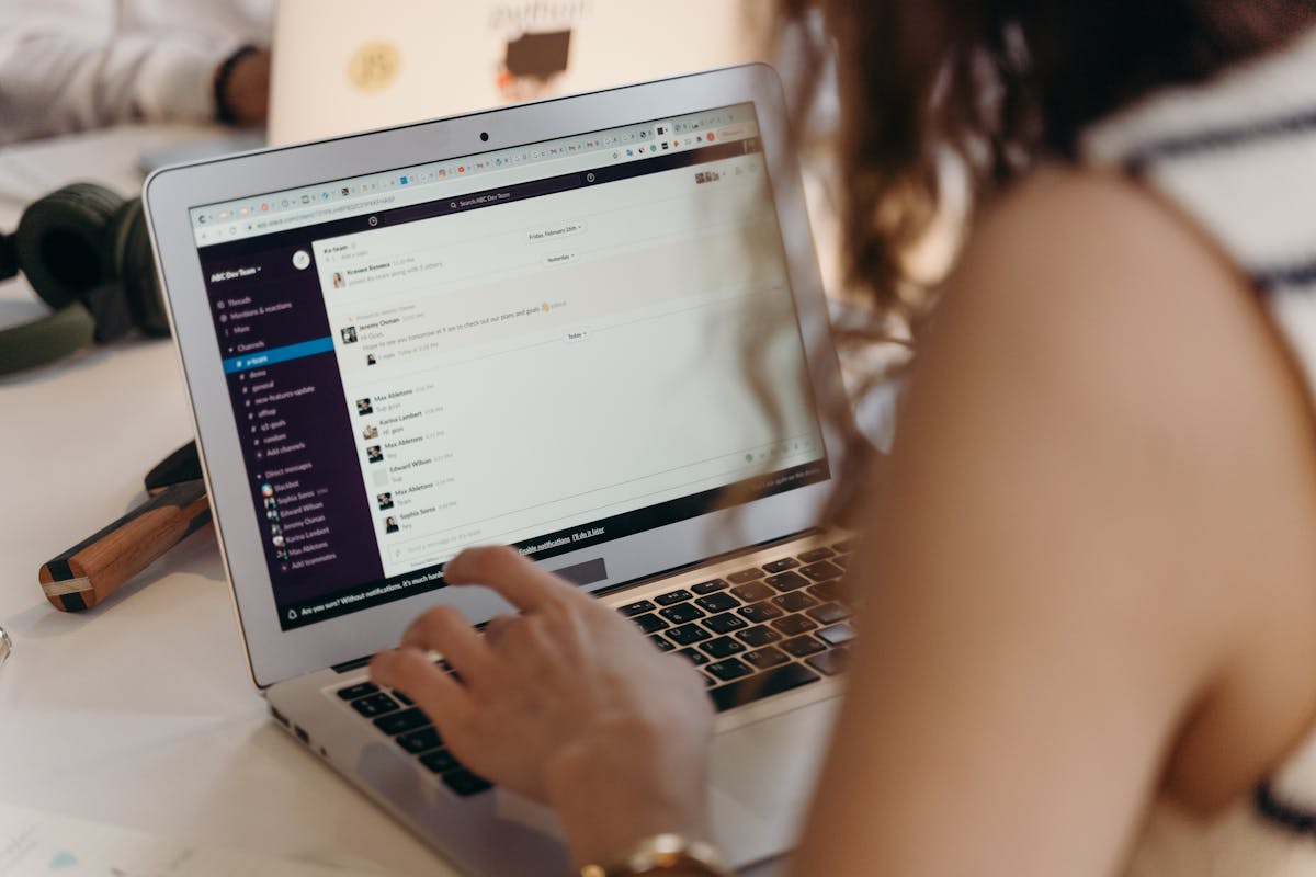 A Importância do Atendimento ao Cliente Durante o Período de Alta Demanda A businesswoman typing on a laptop in an office setting, using Slack for communication.
