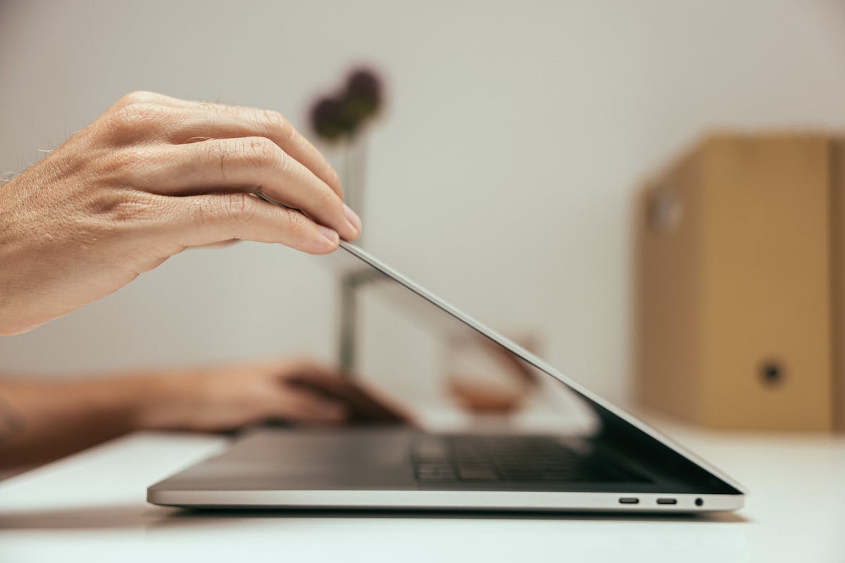 Qual a importância de bater ponto na empresa? A close-up of a hand closing a laptop in a clean and minimal office setting, symbolizing the end of a work session.