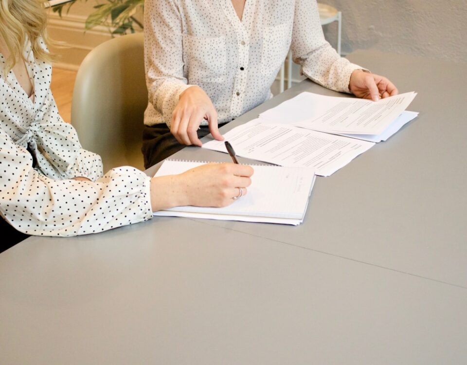 Logística na regularização de documentos para compra e venda de imóveis woman signing on white printer paper beside woman about to touch the documents