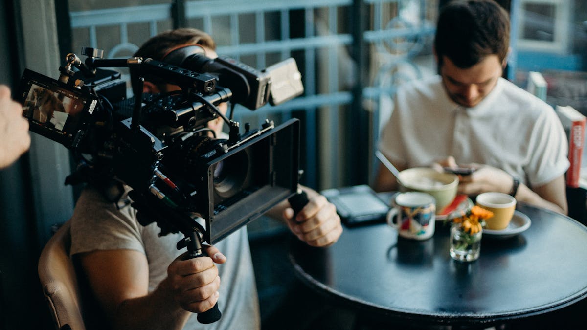 Filmes online impulsionam vendas de eletrônicos Cameraman filming a scene in a cozy cafe setting, capturing the cinematic atmosphere.