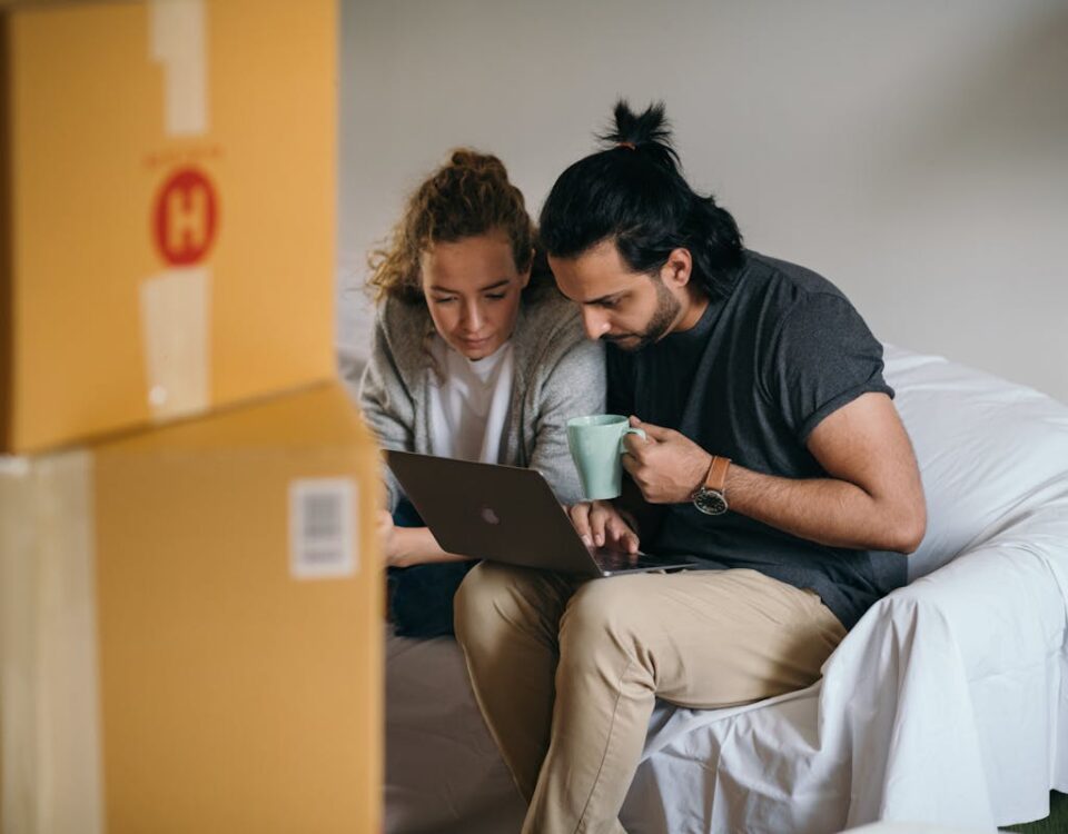 Tendências no mercado de e-commerce imobiliário Couple surrounded by boxes checks laptop details on moving day.