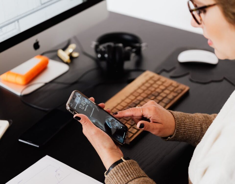 CNH digital: Como usá-la para compras e validações online Professional woman multitasking on smartphone and computer at her desk in an office setting.