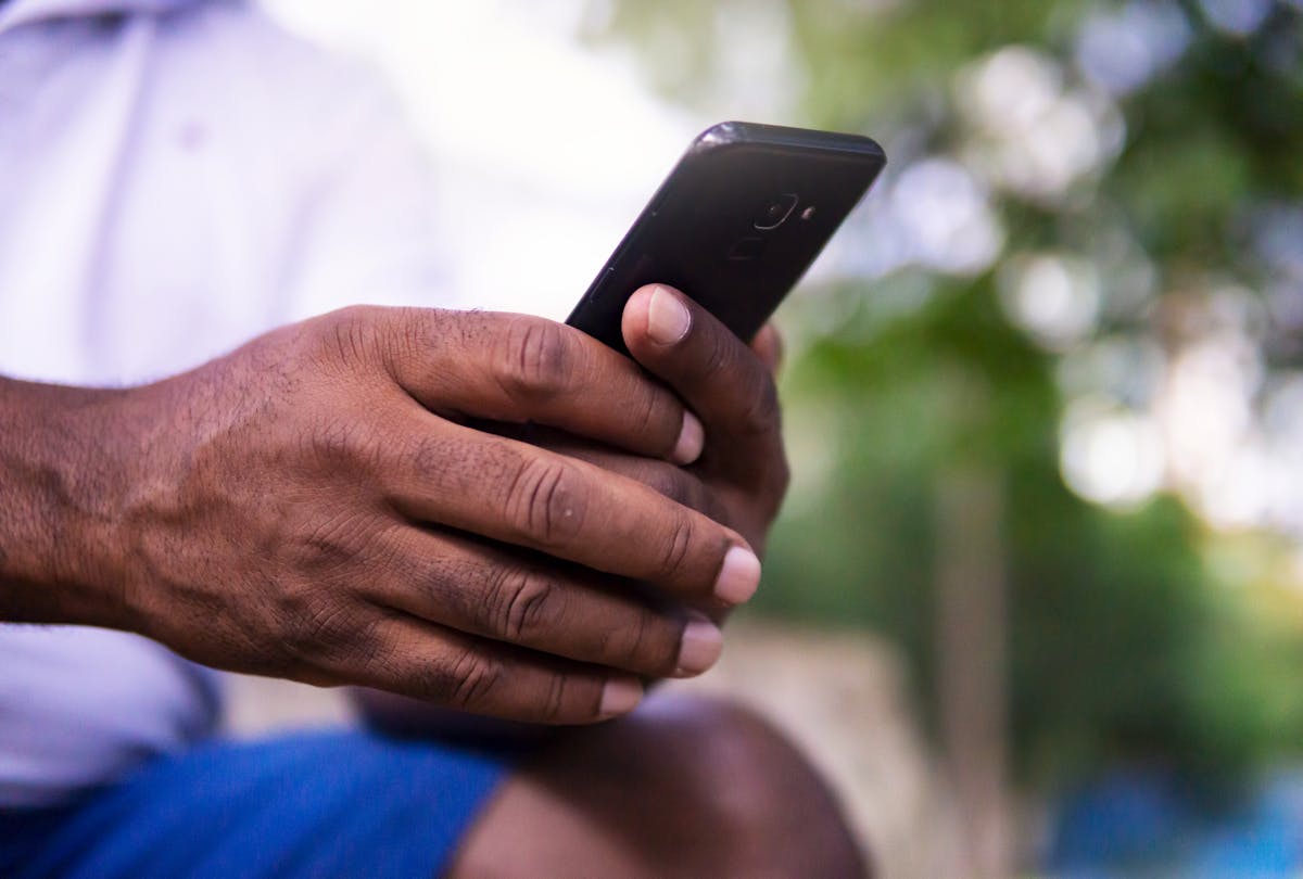 A close-up of a man's hands holding a smartphone in a park setting, showcasing technology use.