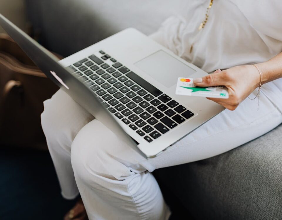 Sites que influenciam a experiência de compra online Adult using laptop and holding bank card for online shopping indoors.