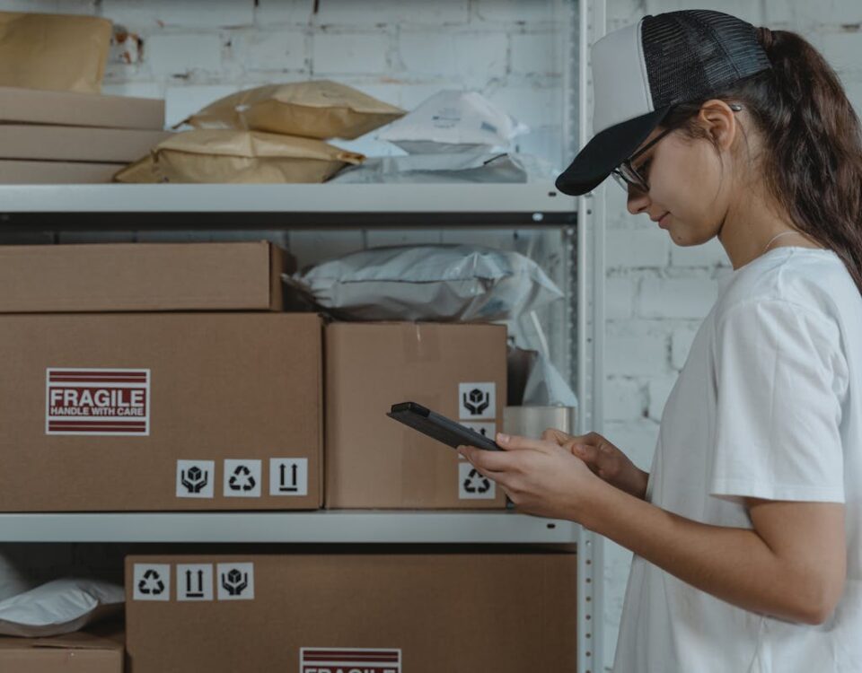 O que conecta inovação e praticidade na logística moderna? A female courier in uniform managing packages with a device in a storage room.