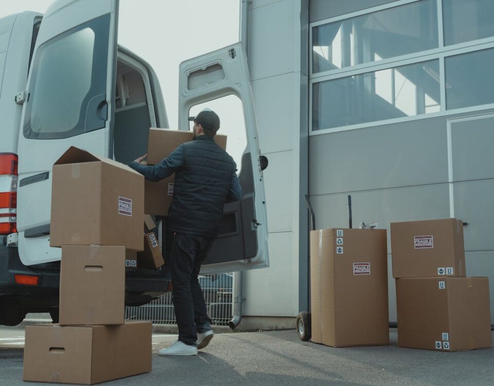 O impacto do seguro nas entregas de e-commerce A delivery man unloading cardboard boxes from a van at a warehouse during the day.