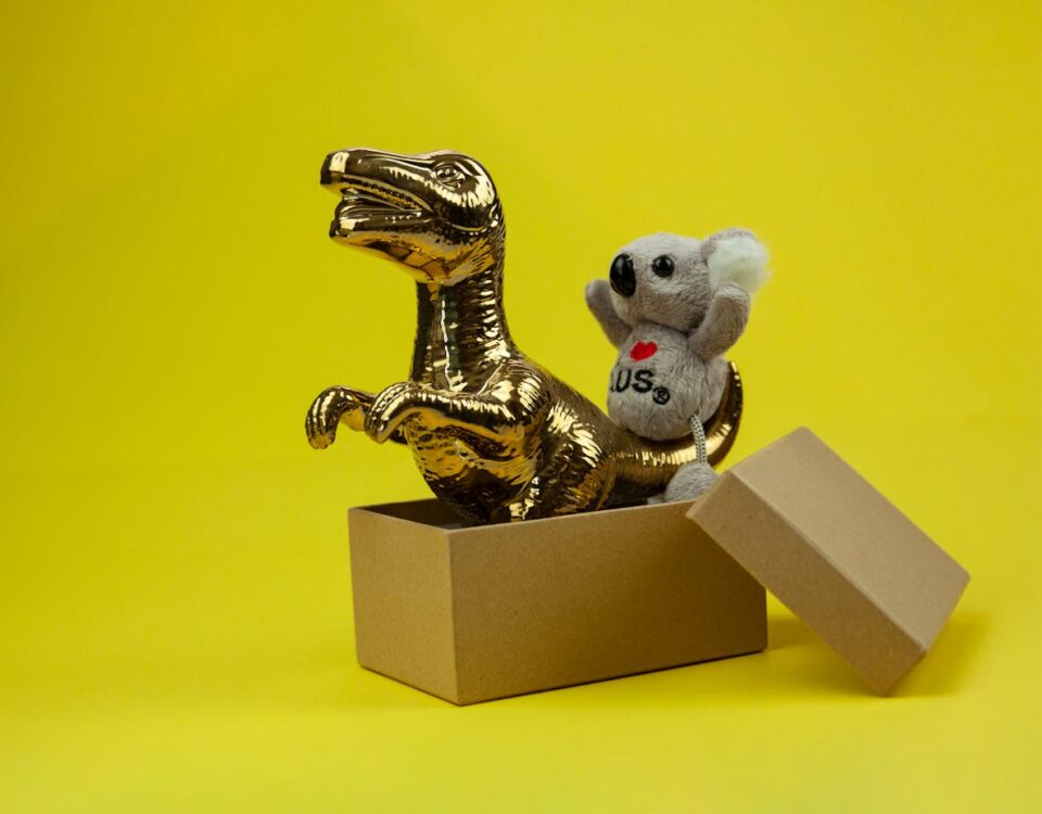 Como as lojas de souvenires estão inovando no e-commerce A golden dinosaur and koala toy in an open box with a vibrant yellow backdrop.