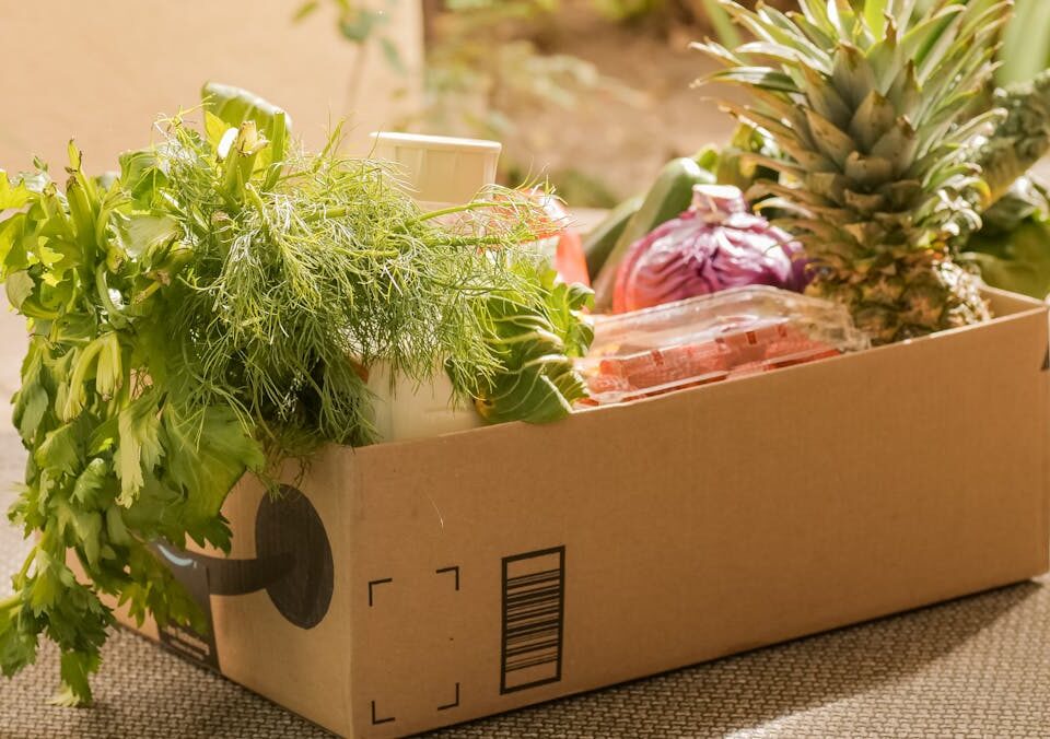 O boom de produtos focados em dieta para DII no e-commerce A cardboard box filled with fresh vegetables and fruits, perfect for delivery or online shopping.