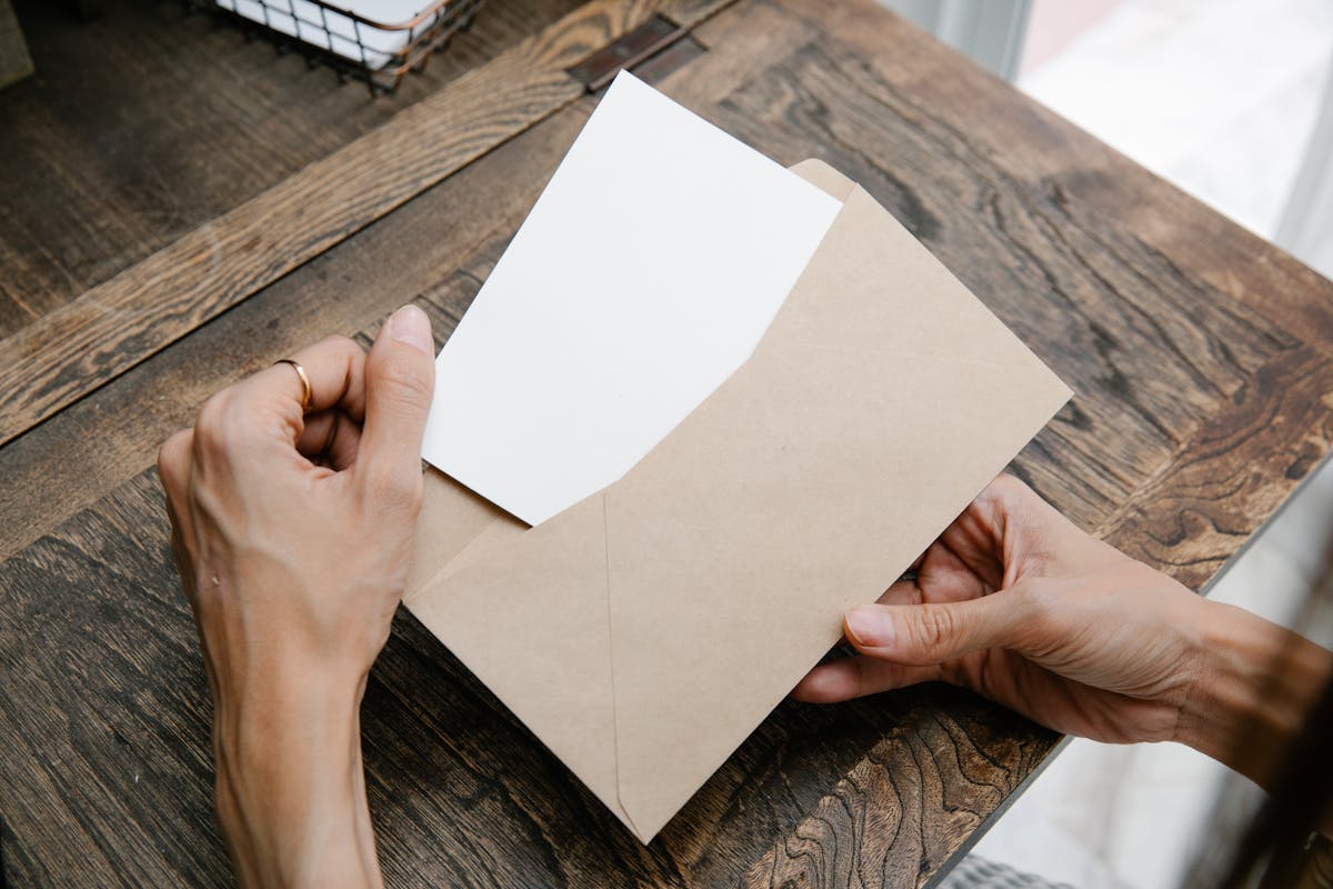 Entrega da CNH: O que motoristas precisam saber Hands holding a letter inside a brown envelope on a wooden desk, viewed from above.