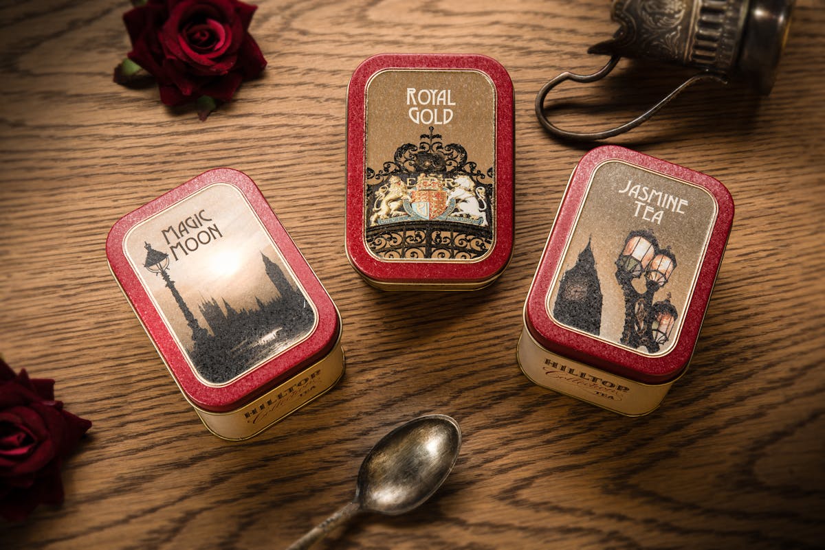 Como as lojas de souvenires estão inovando no e-commerce Top view of three elegant tea tins with labels, accompanied by a vintage spoon, on a wooden surface.