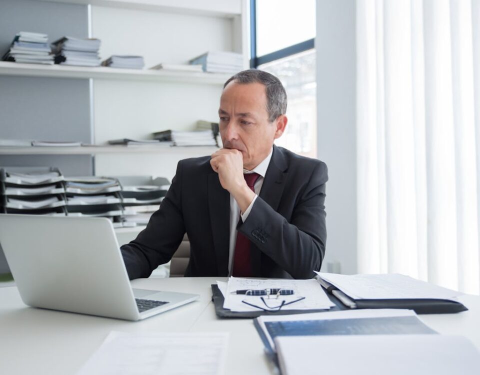 Advogados criminalistas e o uso de plataformas de e-commerce Mature business executive thoughtful at desk with laptop and documents in modern office setting.