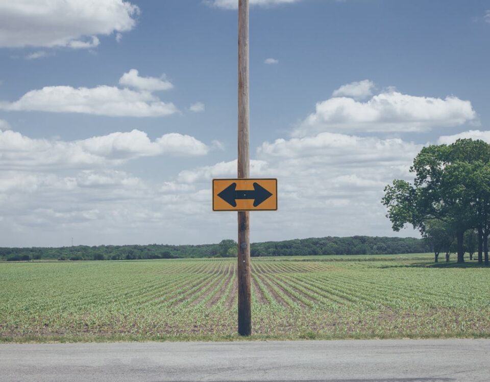 Como empresas especializadas fazem sinalização viária eficiente Scenic rural road sign on farmland with clear blue sky and clouds.