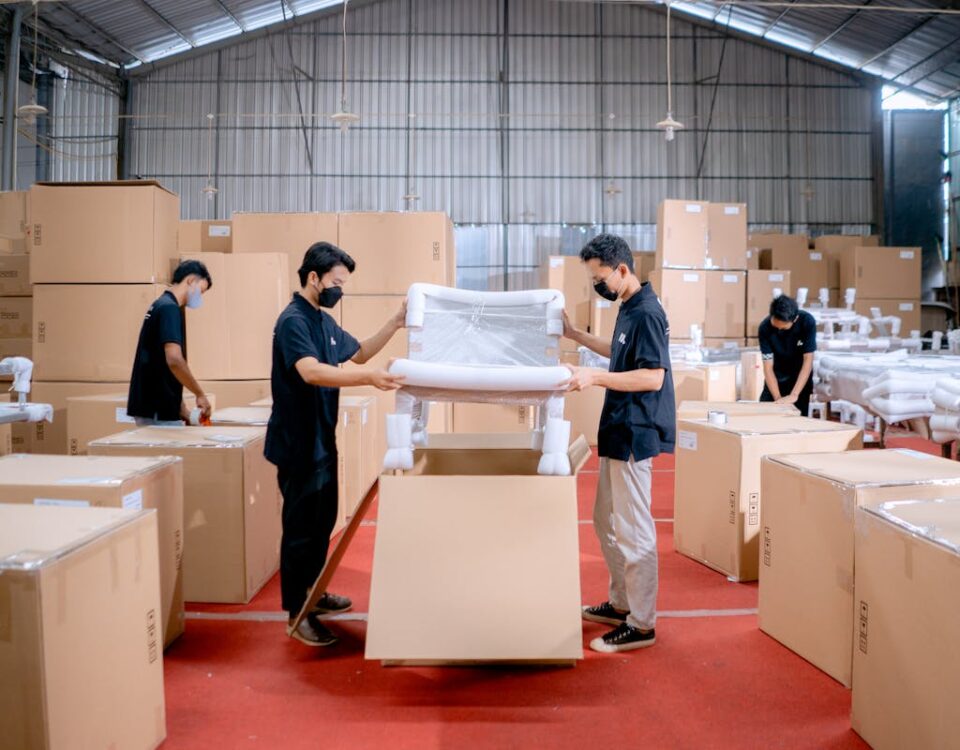 Logística na entrega de móveis de luxo: O que considerar Men in a warehouse wearing masks, assembling and packing furniture into boxes with efficiency.