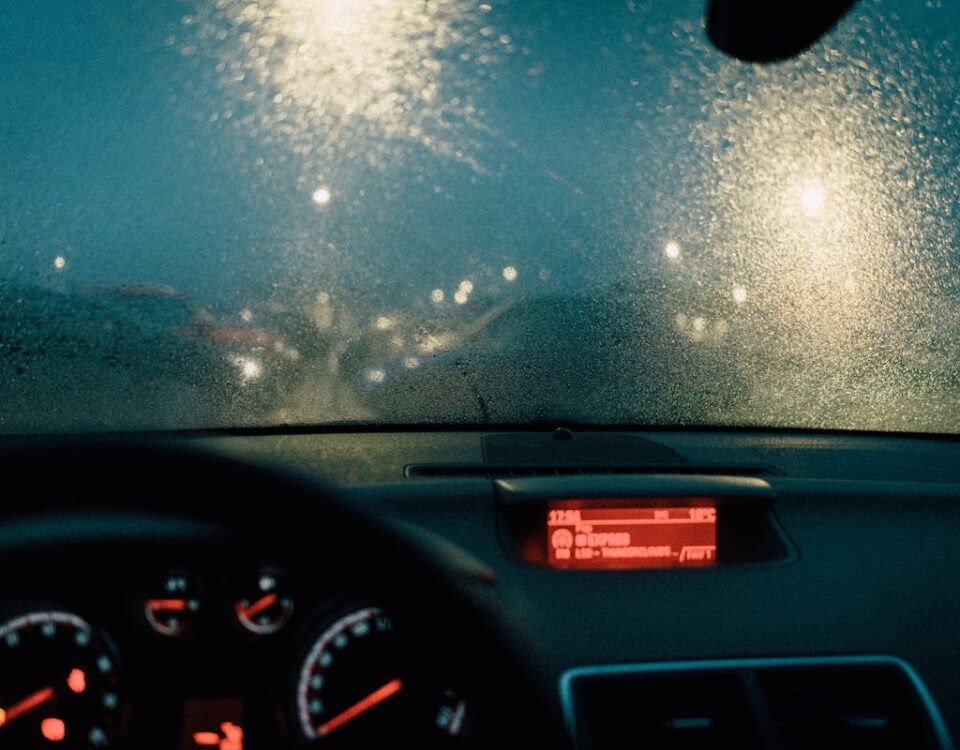 Direção noturna: desafios e dicas para entregadores View from car interior with raindrops on windshield and blurred lights at night.