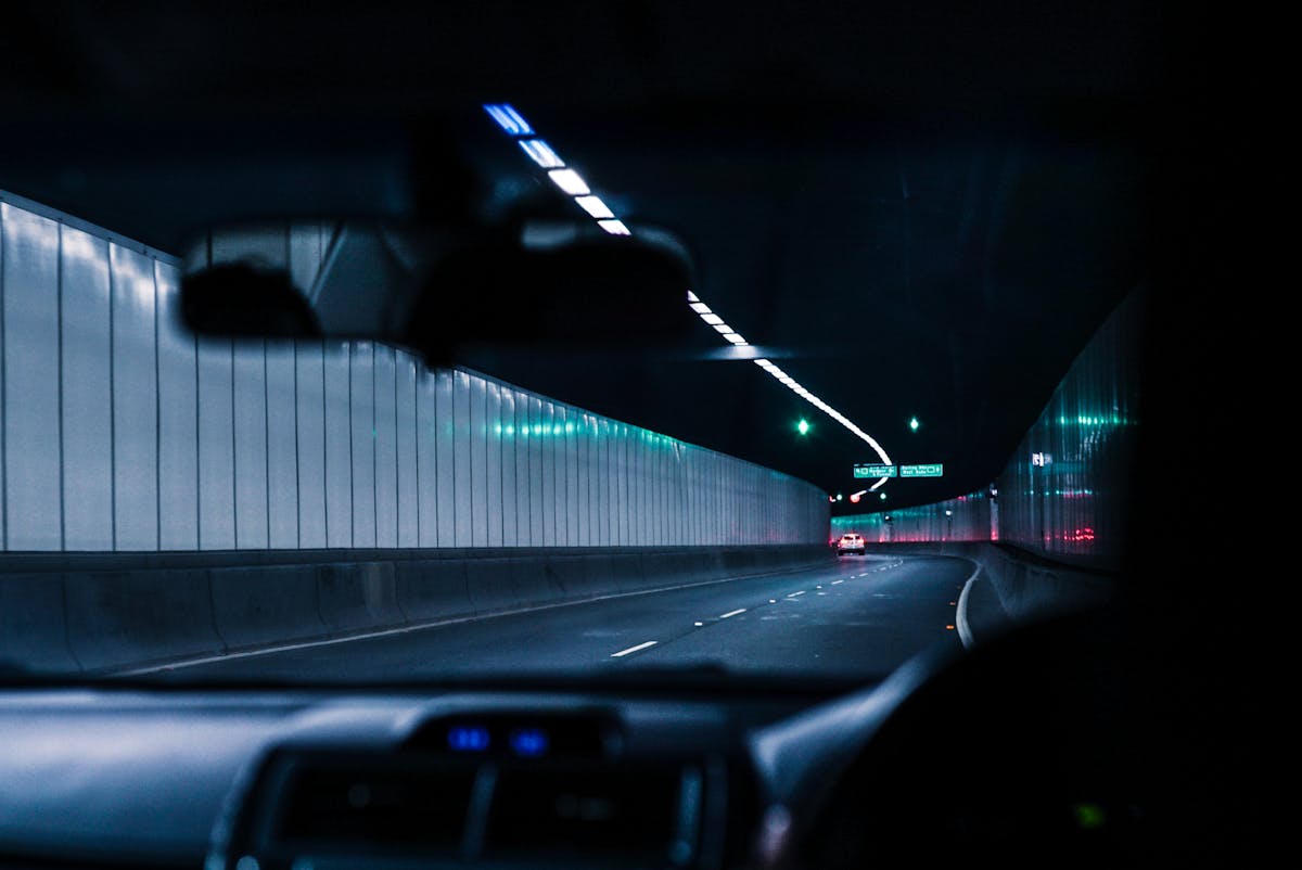 Direção noturna: desafios e dicas para entregadores Inside view of a car driving through a brightly lit urban tunnel at night, showcasing modern transportation.