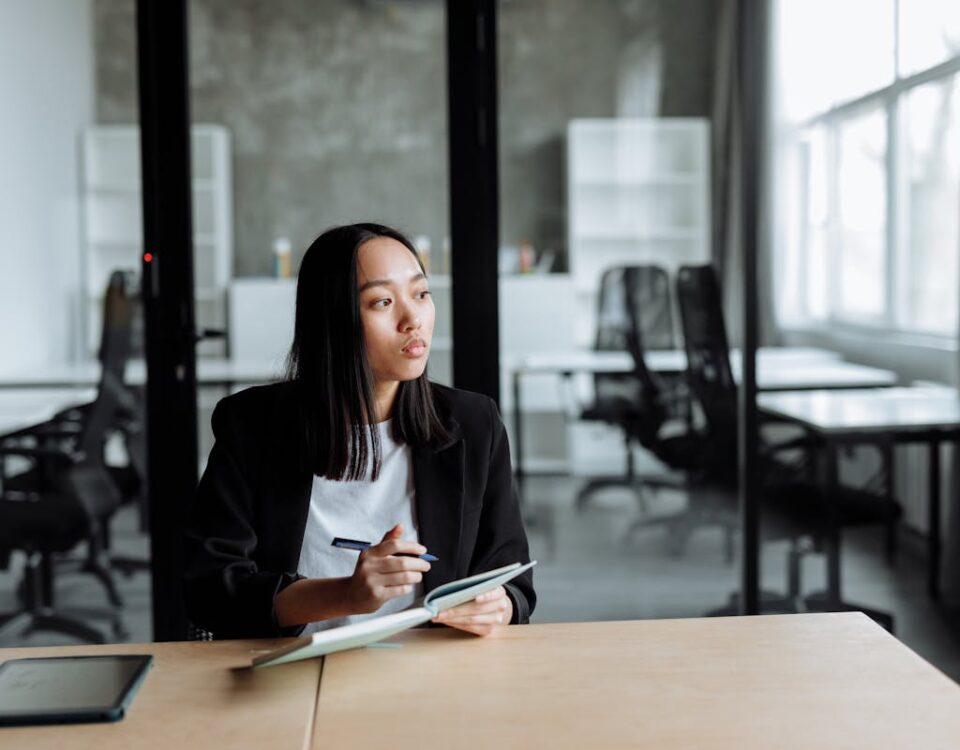Como empresas de TI otimizam a logística de serviços Portrait of a woman in a modern office pondering ideas, holding a notebook and pen.