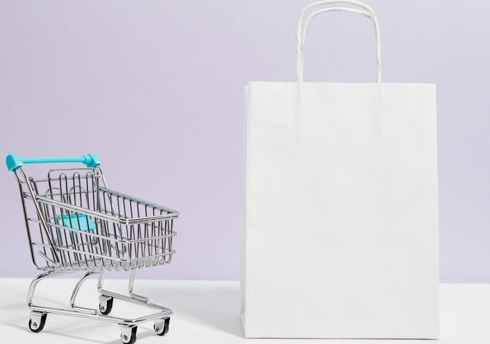 Carrinho de compras em miniatura ao lado de uma sacola de papel branca