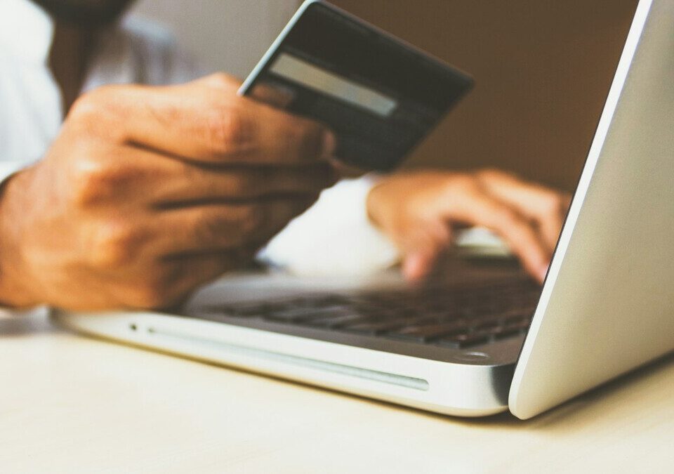 Pessoa usando notebook com cartão de crédito na mão para compra online